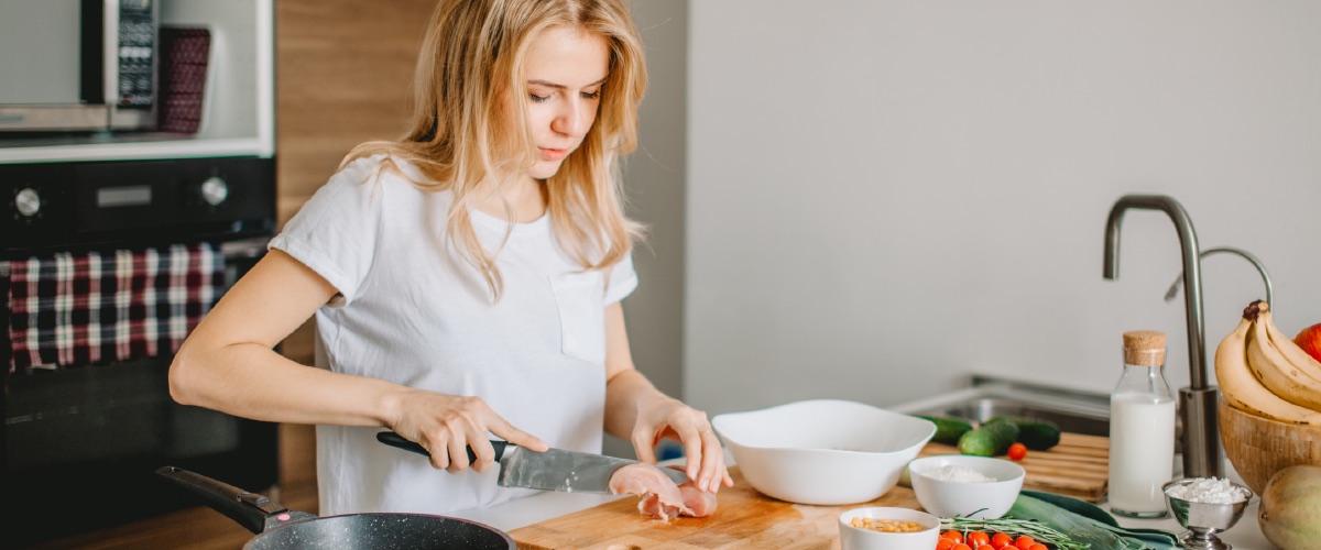 Person preparing a meal at a kitchen worktop surrounded by fresh vegetables